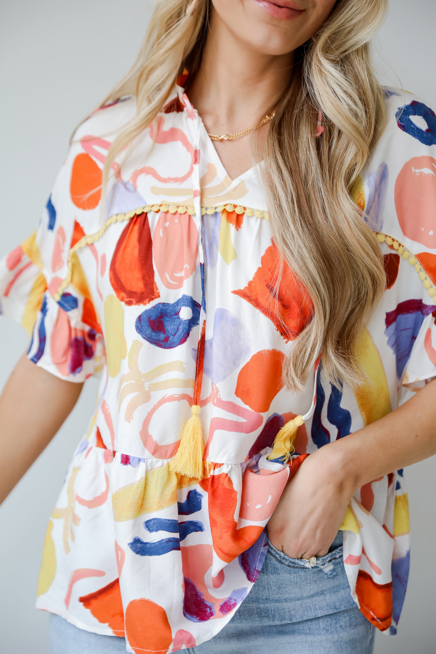 Breezy Sophistication Ivory Ruffle Blouse. Ivory base with blue and orange prints. Yellow tassel