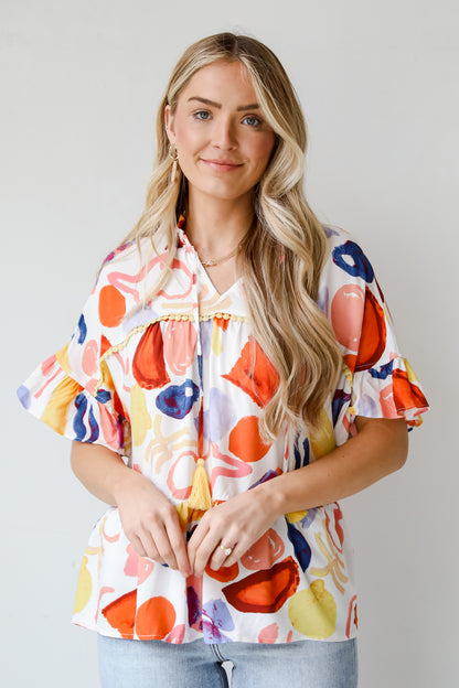 Breezy Sophistication Ivory Ruffle Blouse. Ivory base with blue and orange prints. Yellow tassel